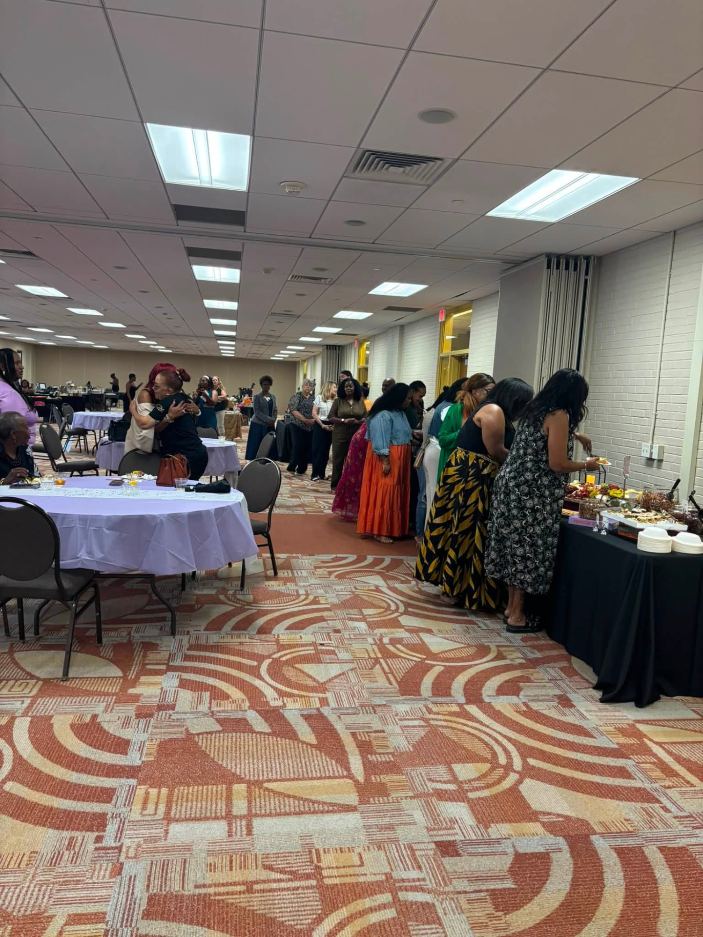 Guests mingling and gathering around the food table in the event hall.